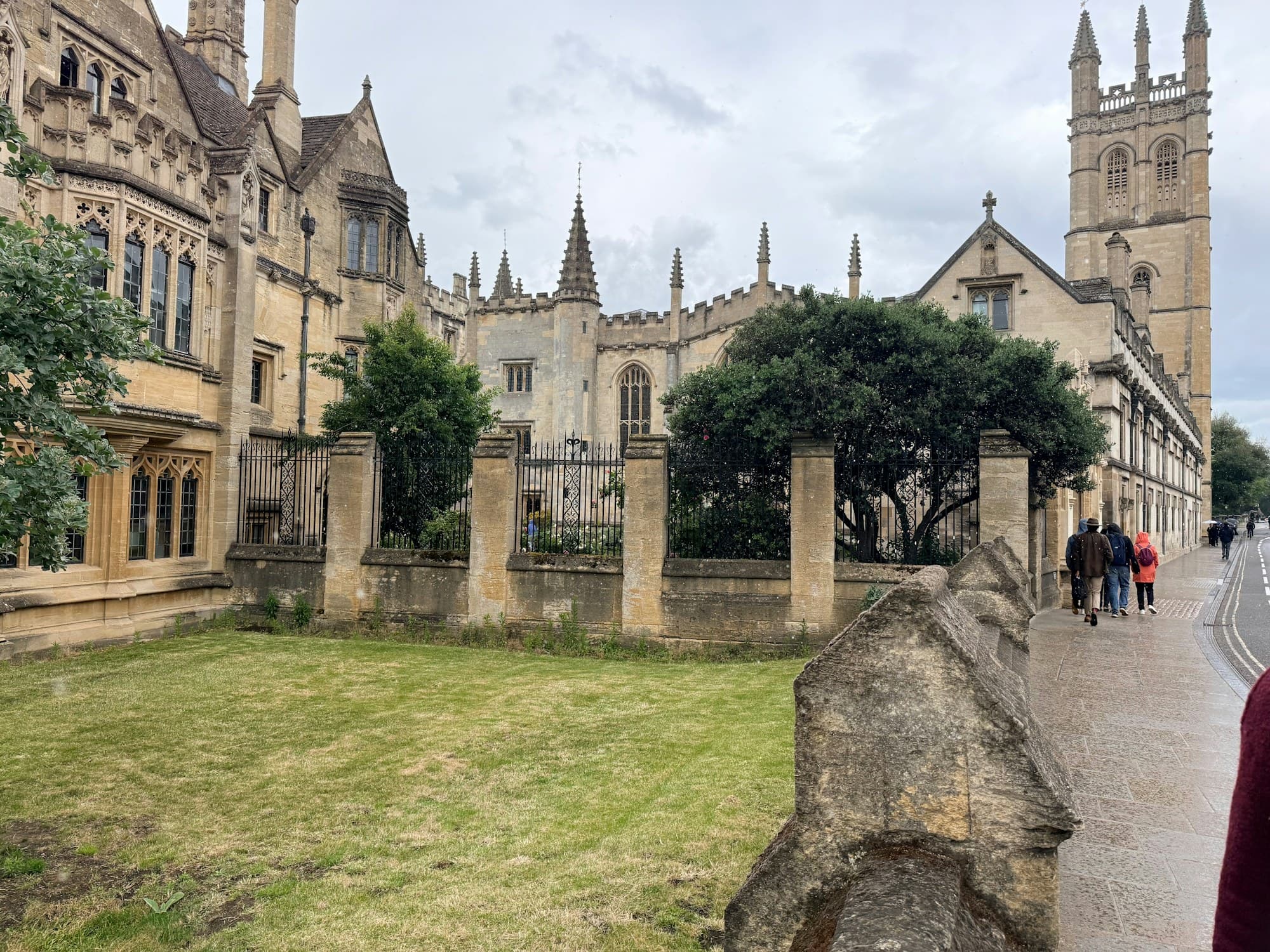 People walking past historic stone university buildings in Oxford on an overcast day
