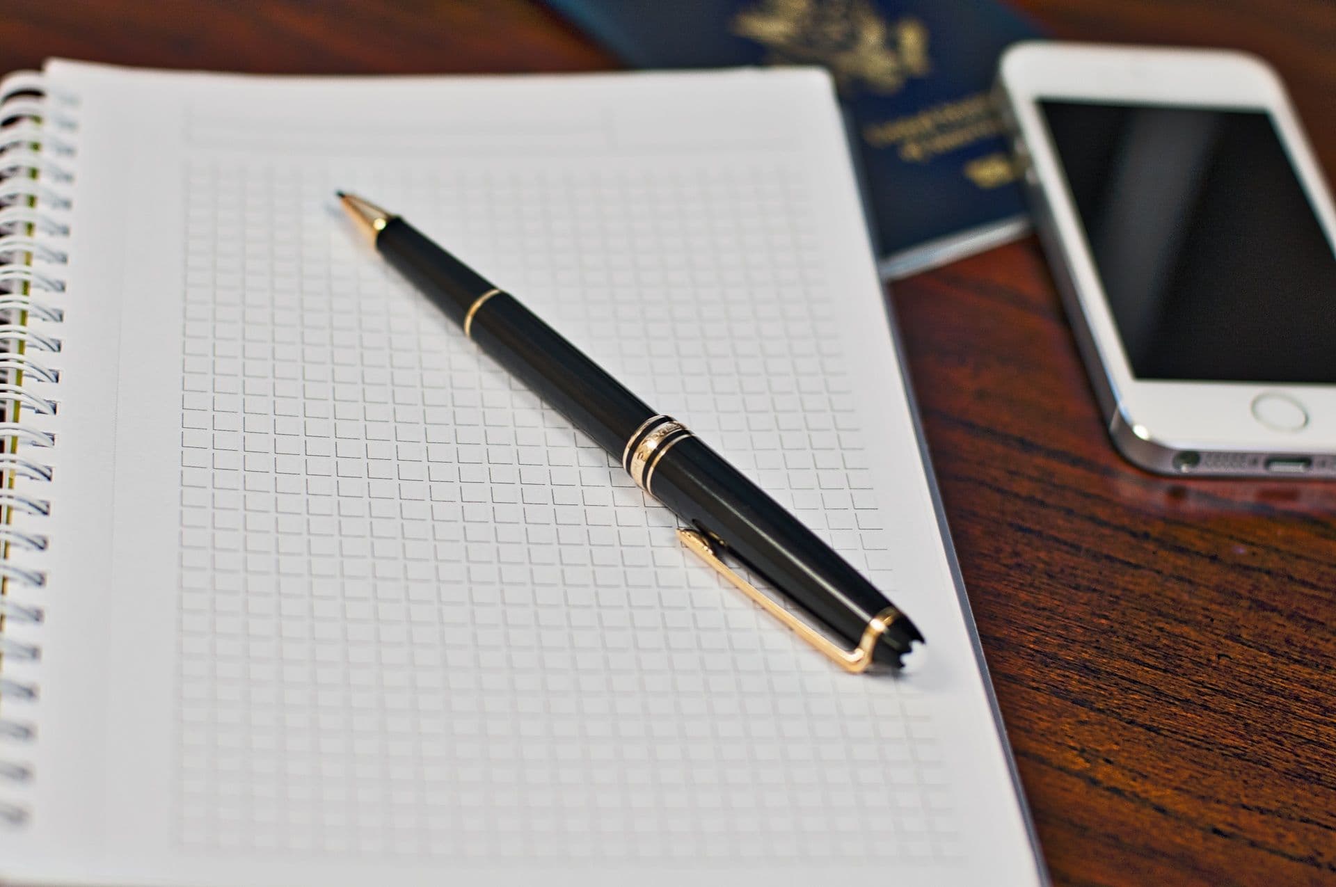 A passport, a phone and a pen on a notebook on a wooden desk