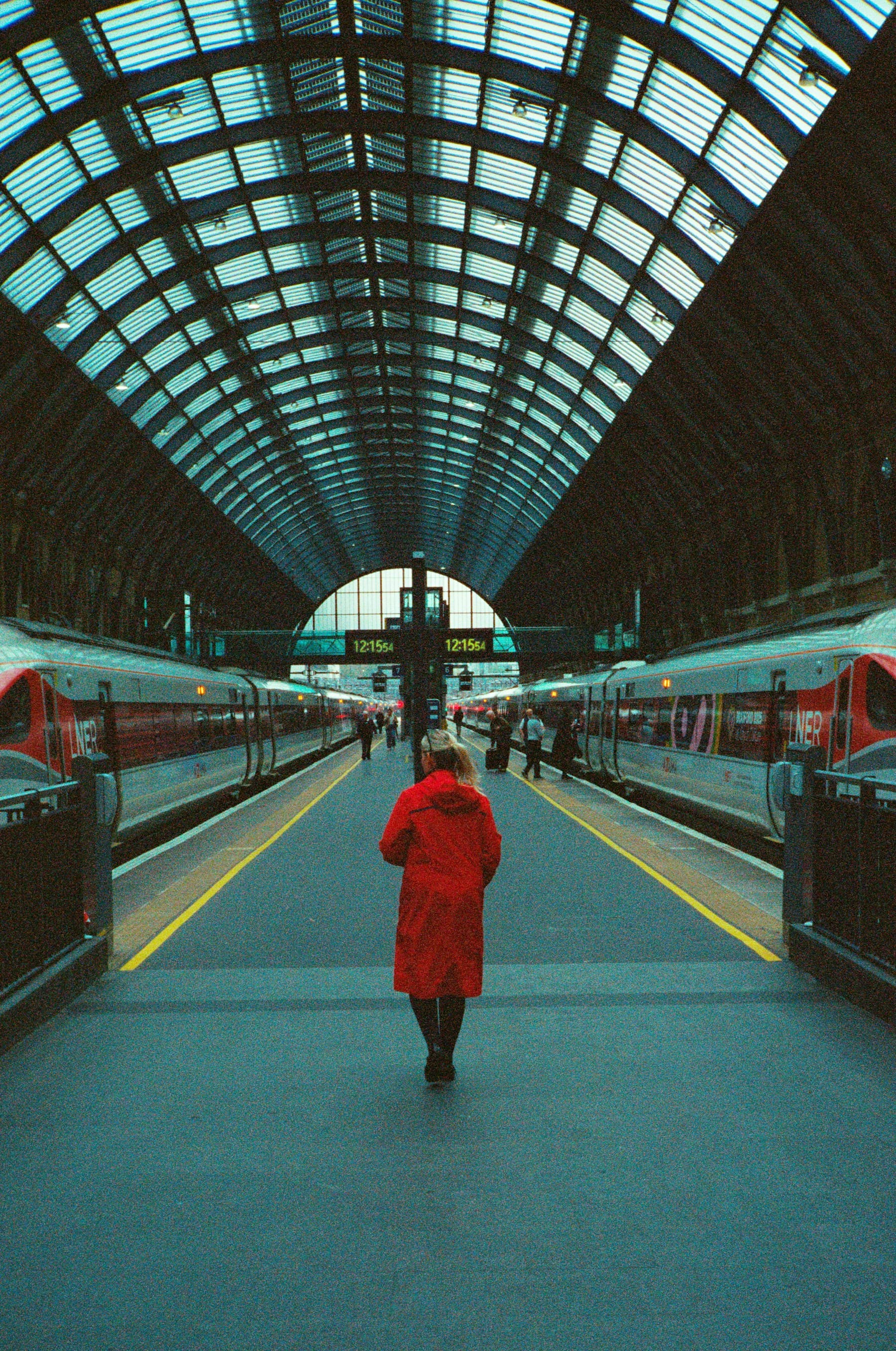 A person in a red coat walking down a platform under the iron roof of a London railway station