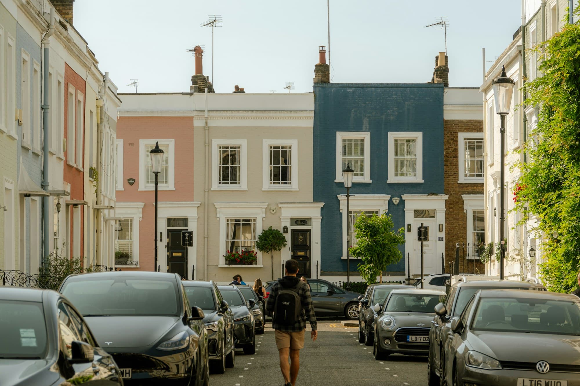 A person with a backpack walking down a street of pastel terraced houses in London